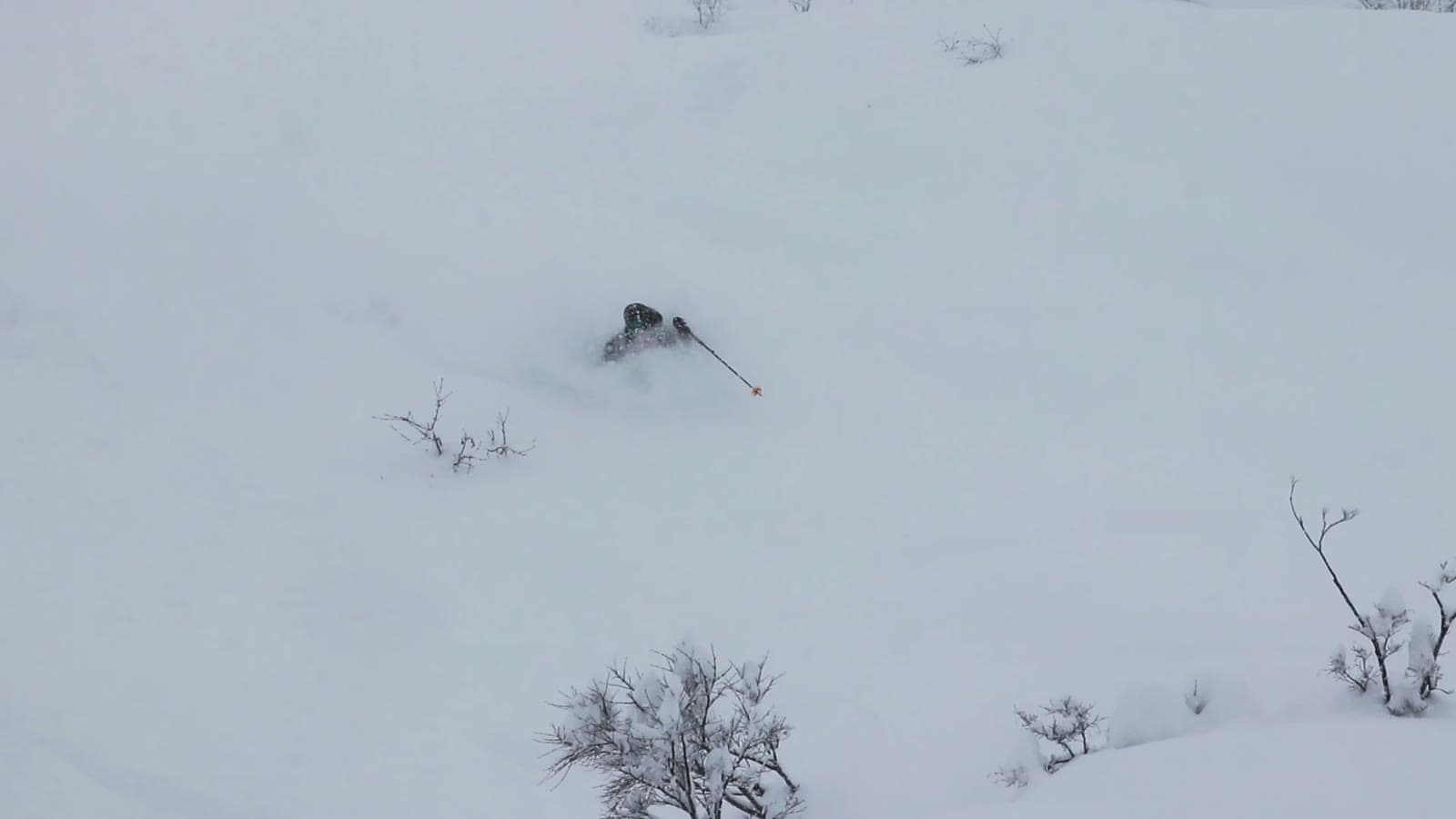 A backcountry skier chest-deep in powder in a whiteout, half-swallowed by snow