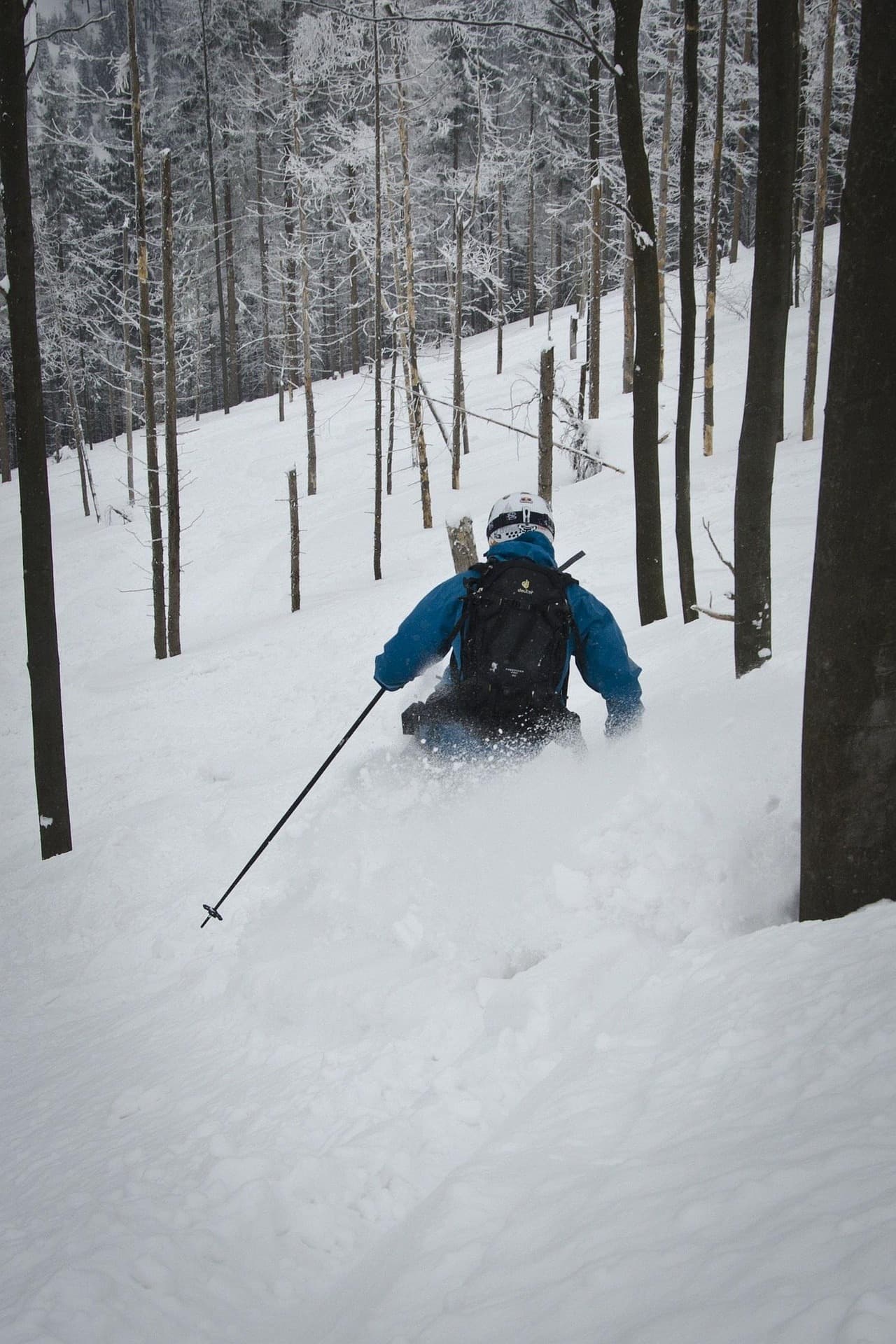 A lone backcountry traveler walking into a darkening, snow-covered hollow at dusk